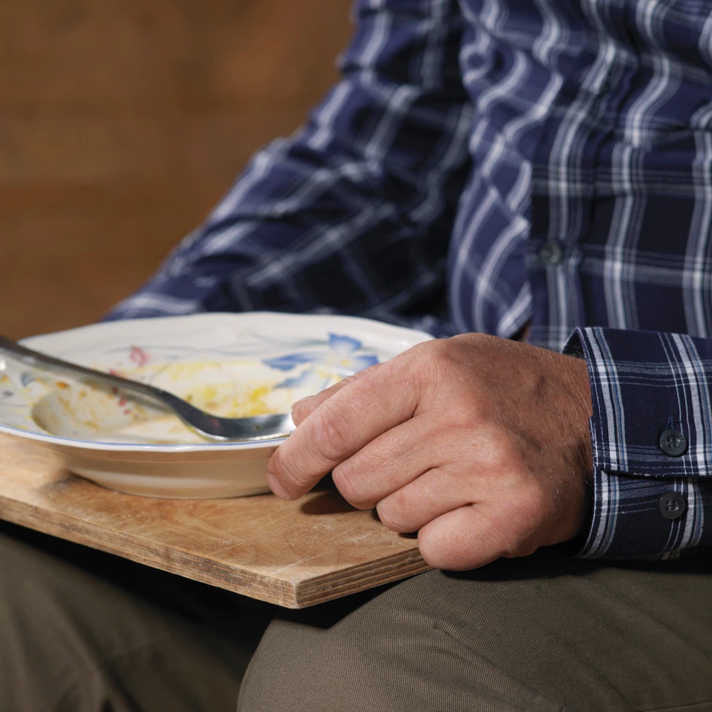 Elderly man sitting and eating from bowl on a tray