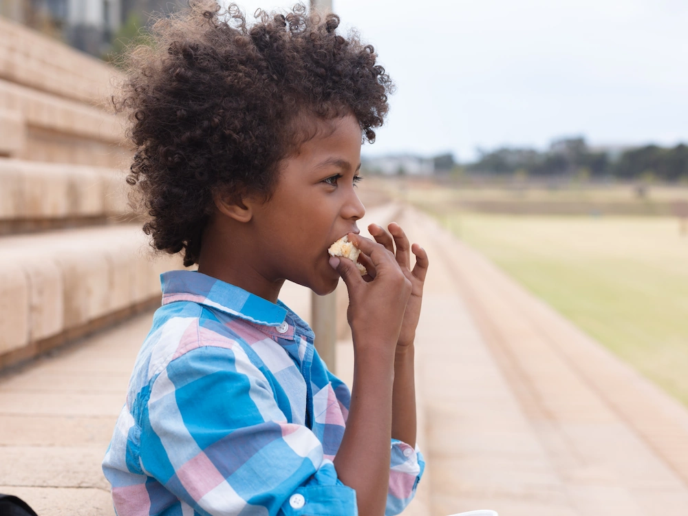 Elementary school boy sitting on bleachers, eating a sandwich